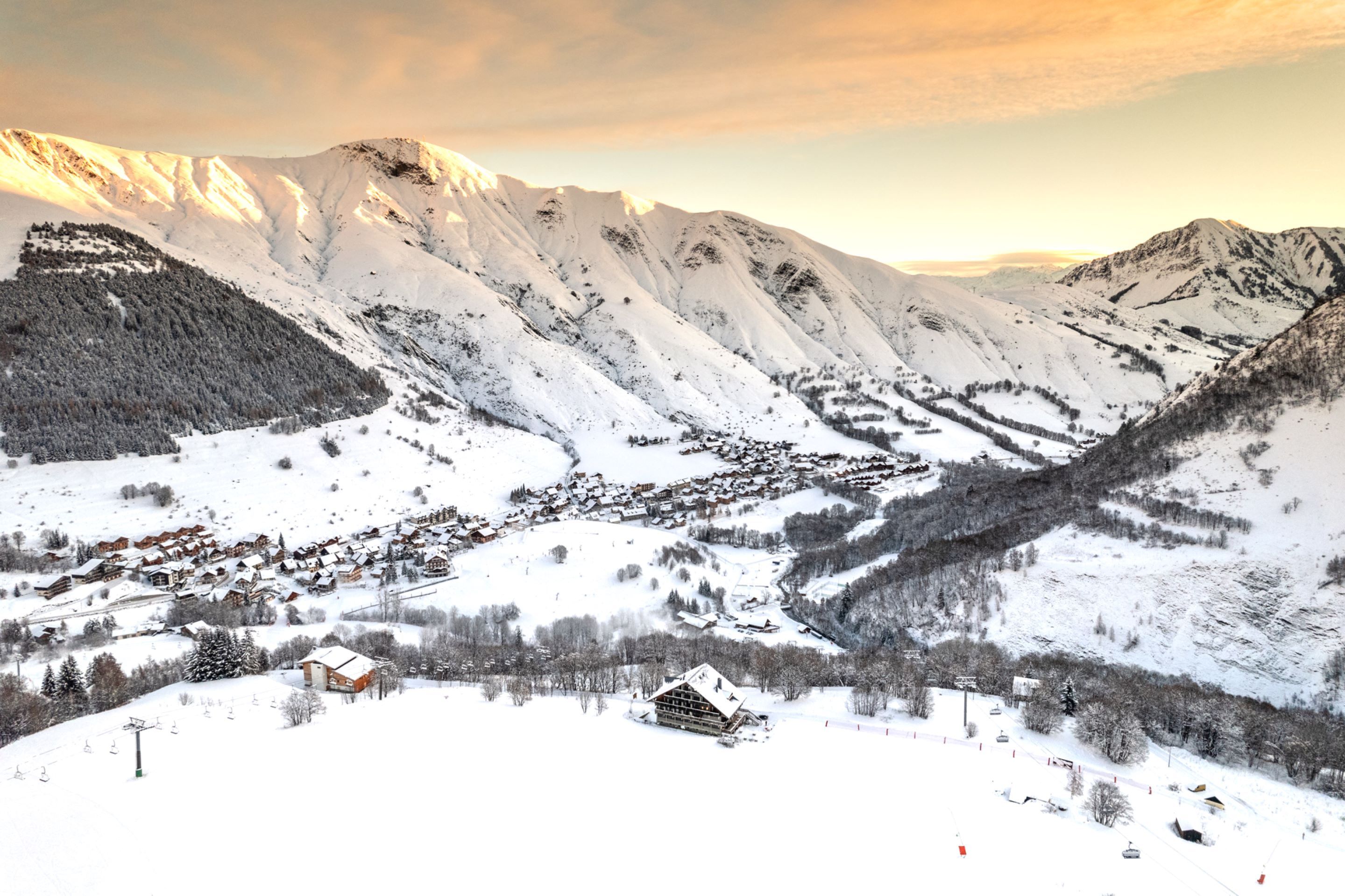 Een besneeuwde bergdorp met traditionele houten huizen, een skilift en een helder uitzicht op de omliggende toppen.