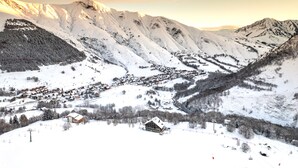 Un village de montagne enneigé, avec ses maisons traditionnelles en bois, un télésiège et une vue dégagée sur les sommets environnants.