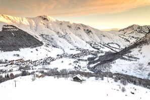 Un village de montagne enneigé, avec ses maisons traditionnelles en bois, un télésiège et une vue dégagée sur les sommets environnants.