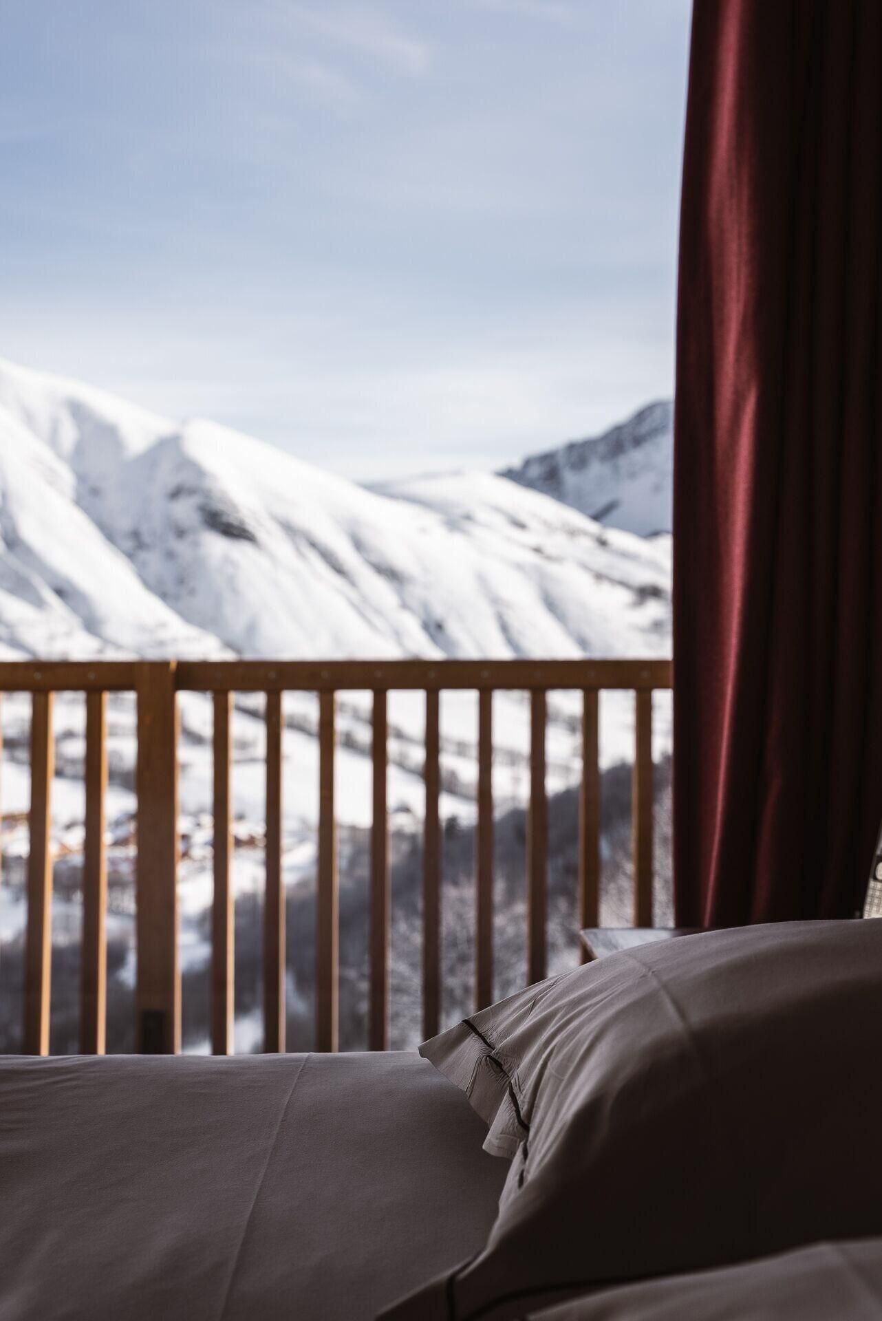A bed with a view of snow-covered mountains through a balcony railing.