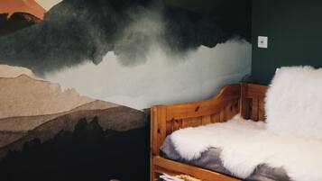 Een kamer met een houten bed, een tafeltje met een mand, en een muurschildering van een berglandschap met vogels.
