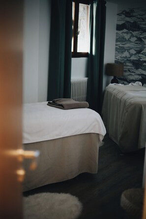 Une chambre d’hôtel avec deux lits, un radiateur, une lampe et un mur décoré d’un motif de montagnes.
