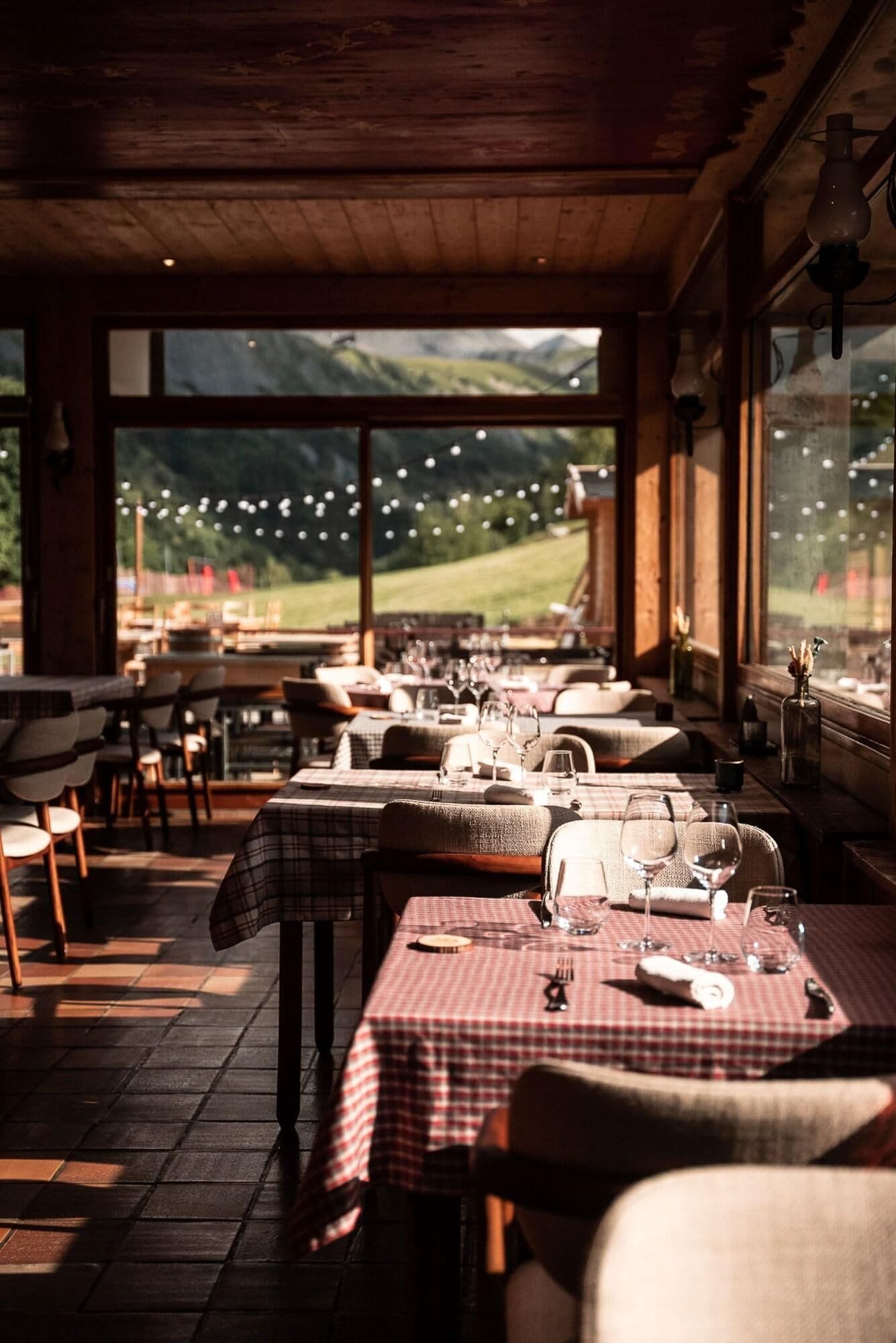 En restaurant med skakternede dugge, træmøbler og store vinduer der giver udsigt over et bjerglandskab.