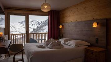 Een slaapkamer met een bed, een bureau, een stoel en uitzicht op met sneeuw bedekte bergen door grote ramen.
