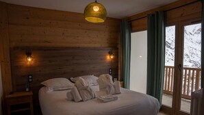 Een slaapkamer met een houten hoofdbord, een bed met witte lakens, twee bedlampen en uitzicht op besneeuwde bergen door een schuifdeur.