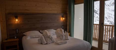A bedroom with a wooden headboard, a bed with white linens, two bedside lamps, and a view of snowy mountains through a sliding door.
