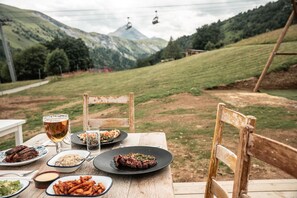 Een buitentafel gedekt met borden eten, bierglazen en een uitzicht op een berglandschap met een skilift op de achtergrond.