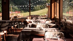 A restaurant with tables set for dining, large windows offering a view of a green landscape, and string lights above the tables. - Les Cedres - Hotel, Restaurant & Spa (Saint-Sorlin-d'Arves)