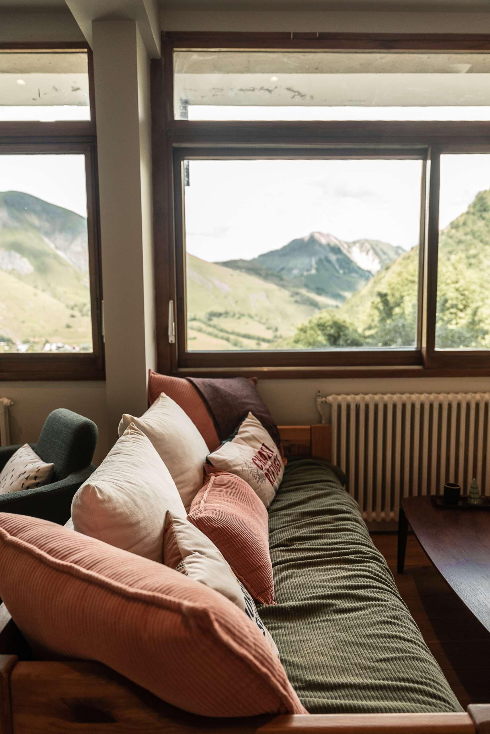 A cozy room with a sofa and chairs facing large windows overlooking a mountainous landscape.