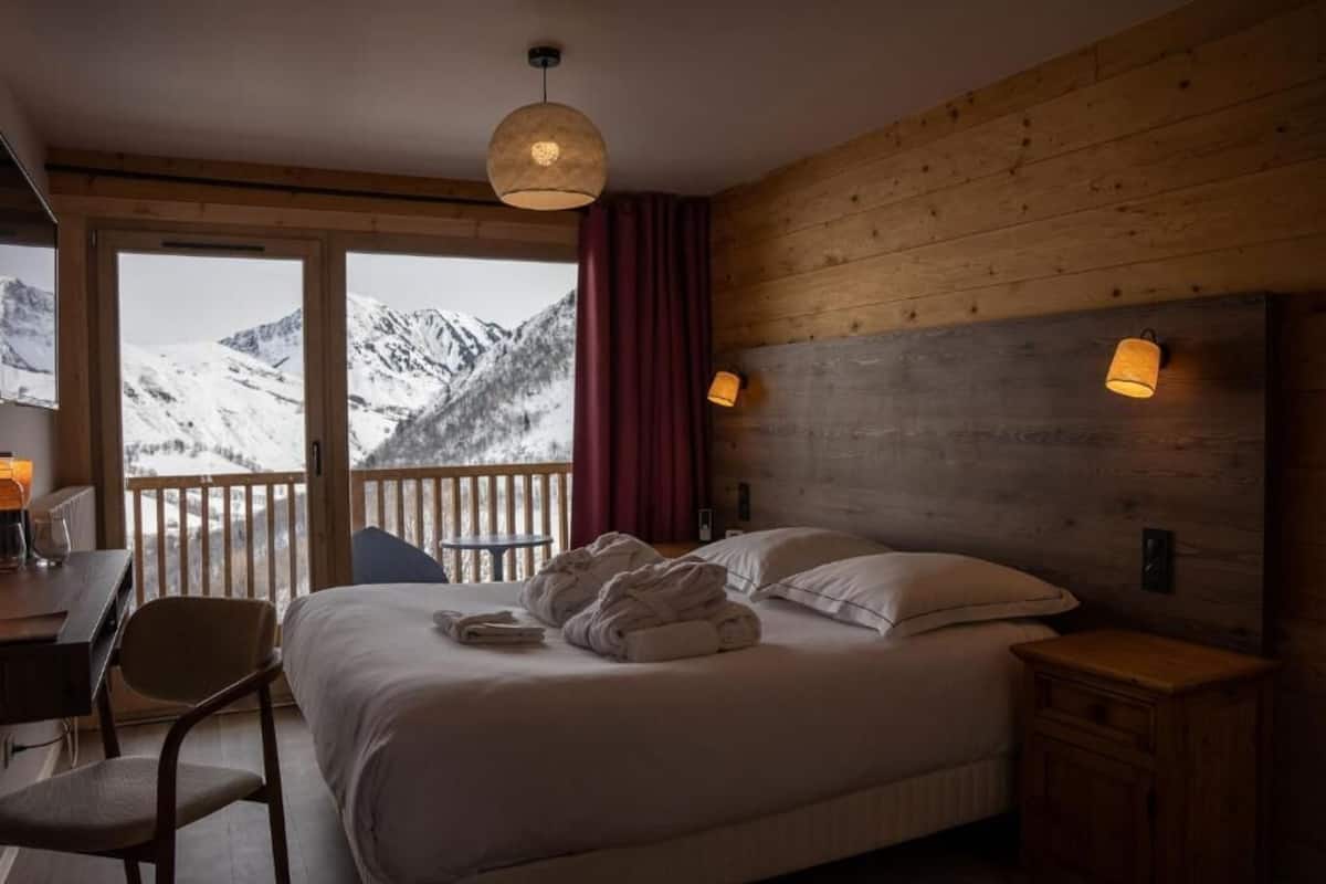Habitación de hotel con cama, escritorio, silla, mesita de noche y vistas a montañas nevadas.