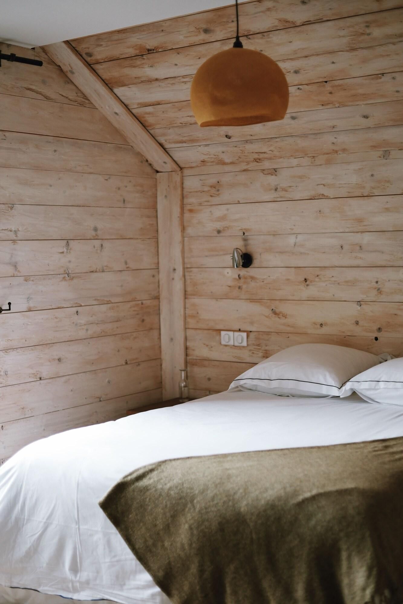 A wooden room with a bed, a hanging pendant light, and a wall socket.