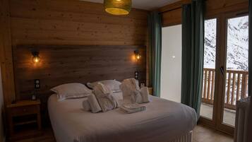 A wooden cabin bedroom with a bed, two bedside lamps, and a view of a snowy landscape through a glass door.