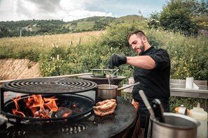 Eine Person kocht draußen mit einem Campingkocher und einem Grill.