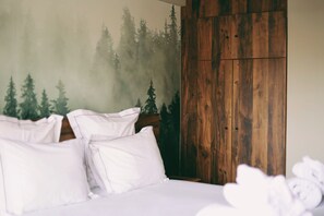 Un lit avec une literie et des oreillers blancs, une armoire en bois et une fresque représentant une forêt sur le mur.