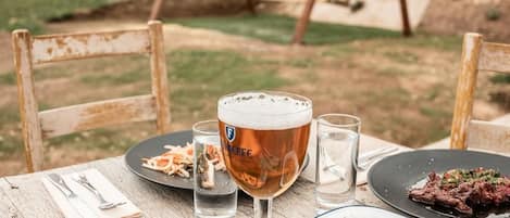 A wooden table set outdoors with plates of food, a beer glass, and a swing set in the background.