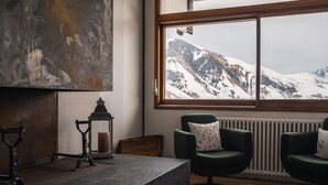 A room with a large window overlooking snow-capped mountains, a stone table, two green armchairs, and a wall-mounted lantern. - Les Cedres - Hotel, Restaurant & Spa (Saint-Sorlin-d'Arves)