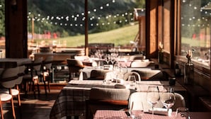 Een restaurant met gedekte tafels, grote ramen met uitzicht op een groen landschap, en lichtslingers boven de tafels.