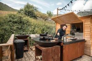 An outdoor cooking area with a grill, a wooden table, and a trash bin. - Les Cedres - Hotel, Restaurant & Spa (Saint-Sorlin-d'Arves)