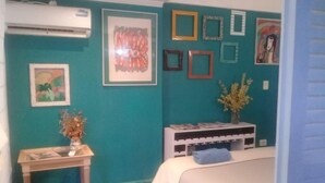 Un dormitorio con paredes verde azulado, una cama con cubrecama blanco, una mesita con un florero de flores secas y un estante con libros y un florero de flores frescas.