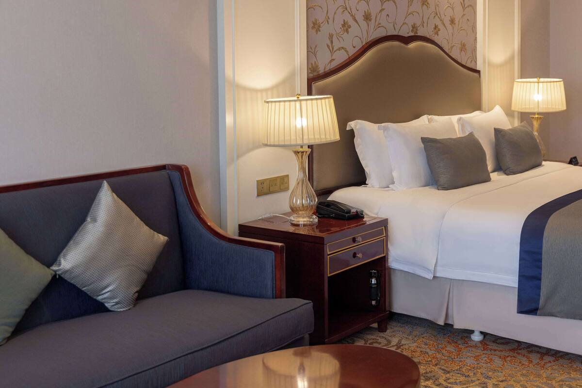 A hotel room with a bed, a sofa, a nightstand with a lamp, and a telephone.