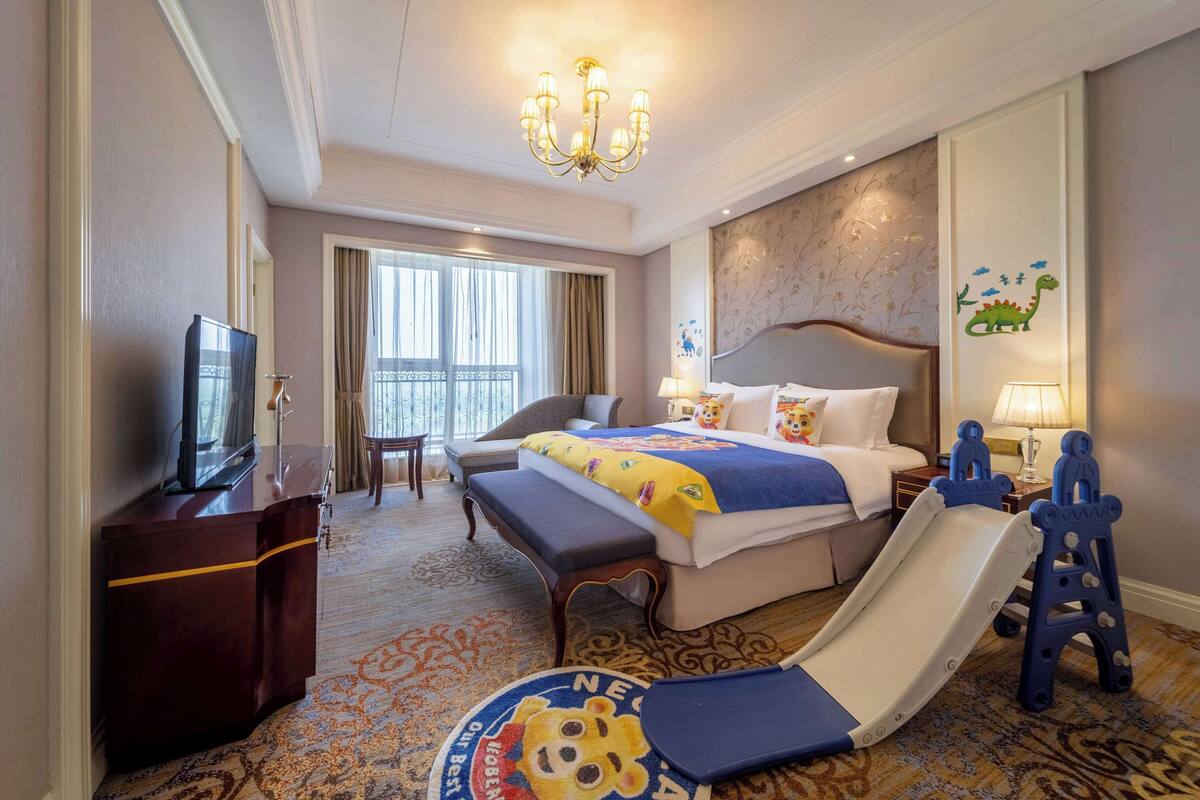 A hotel room with a bed, a desk, a TV, a balcony view, and a children's play area.