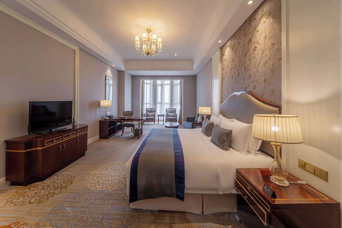 A hotel room with a large bed, a TV, a desk, and a chair.