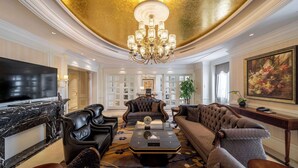 Un salon luxueux agrémenté d’un grand lustre, d’un téléviseur à écran plat, de canapés en cuir et d’une cheminée en marbre.