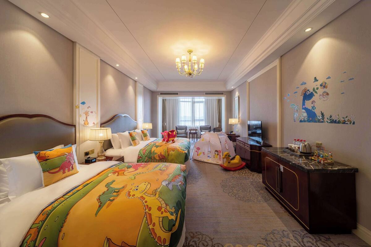 A hotel room with two beds, a desk, a television, and a tent-like play area.