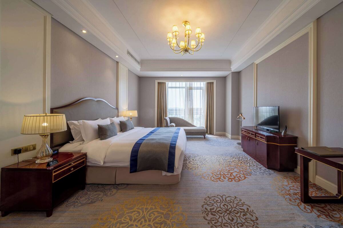 A hotel room with a large bed, a TV, a desk, and a chandelier.