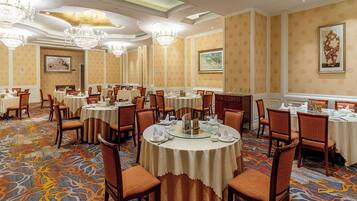 Comedor de hotel con mesas redondas, sillas, candelabros y alfombra estampada.