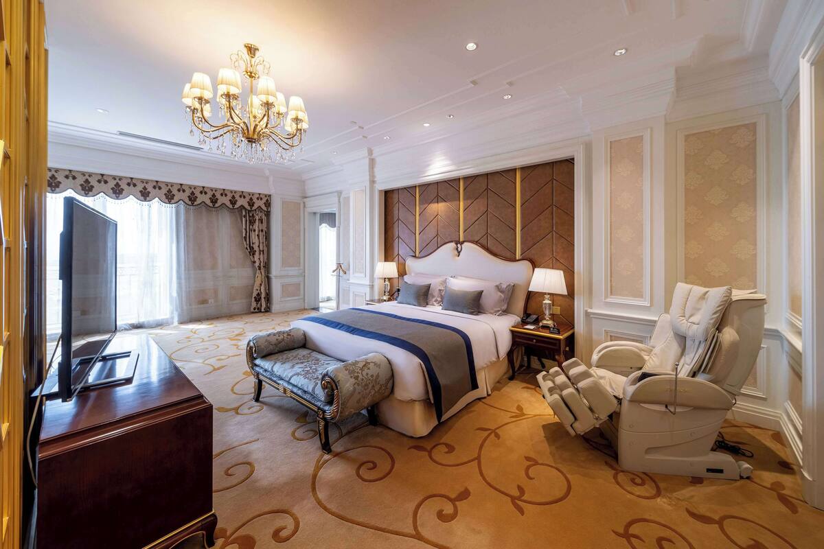 A spacious bedroom with a large bed, a massage chair, a television, and a desk.