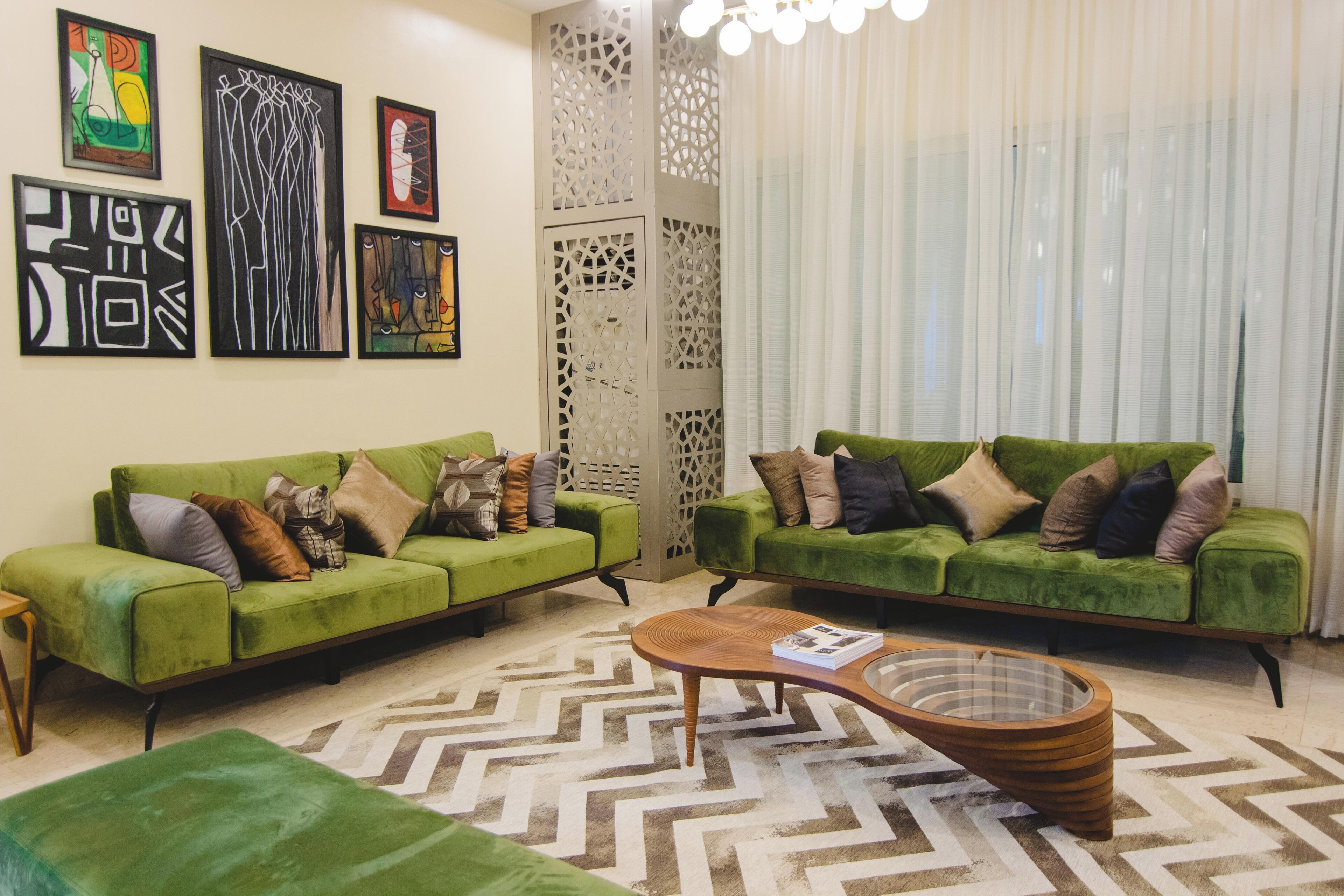 A modern living room with two green sofas, a wooden coffee table, and a geometric patterned rug.