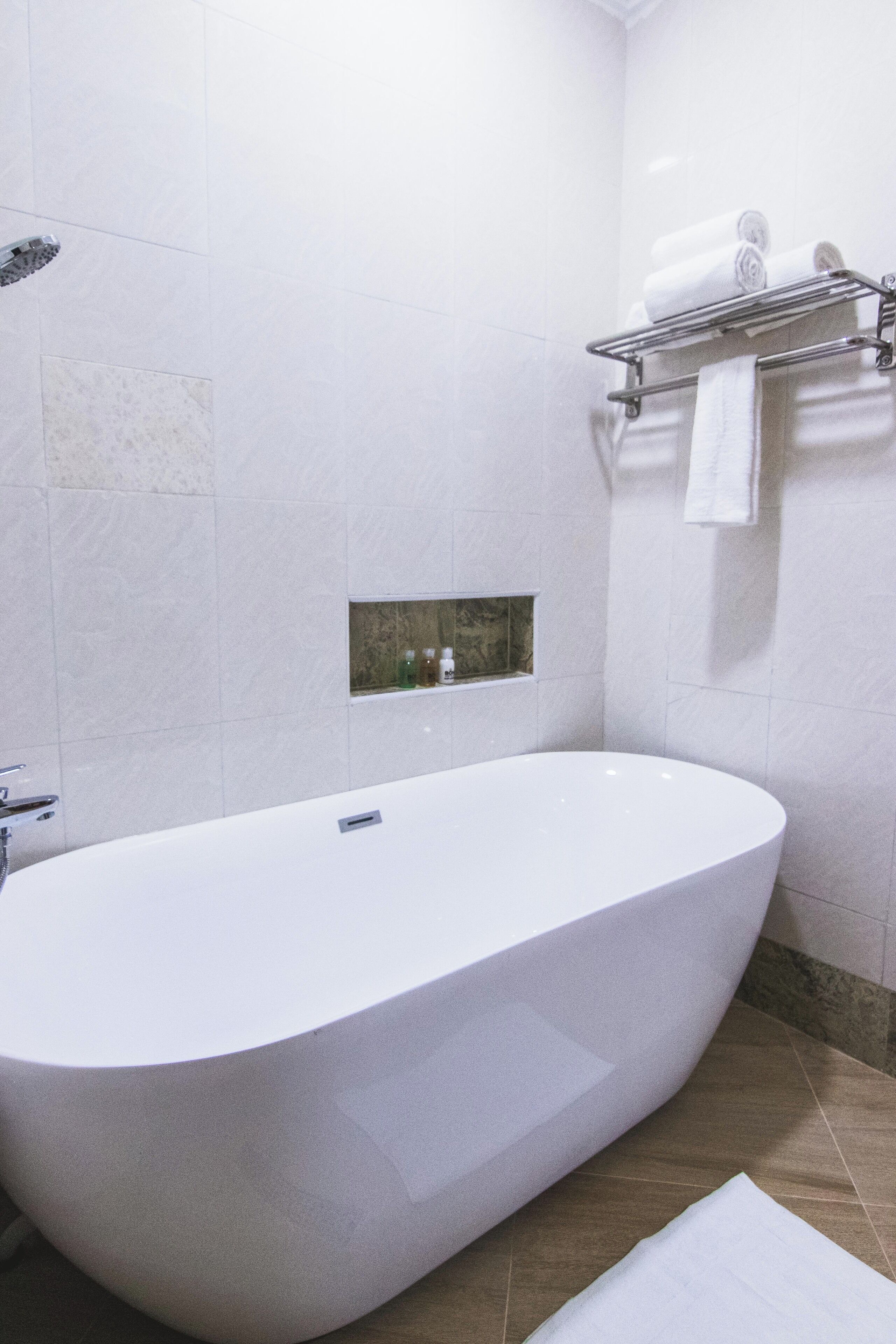 A modern bathroom with a freestanding bathtub, a towel rack with folded towels, and a small shelf with toiletries.