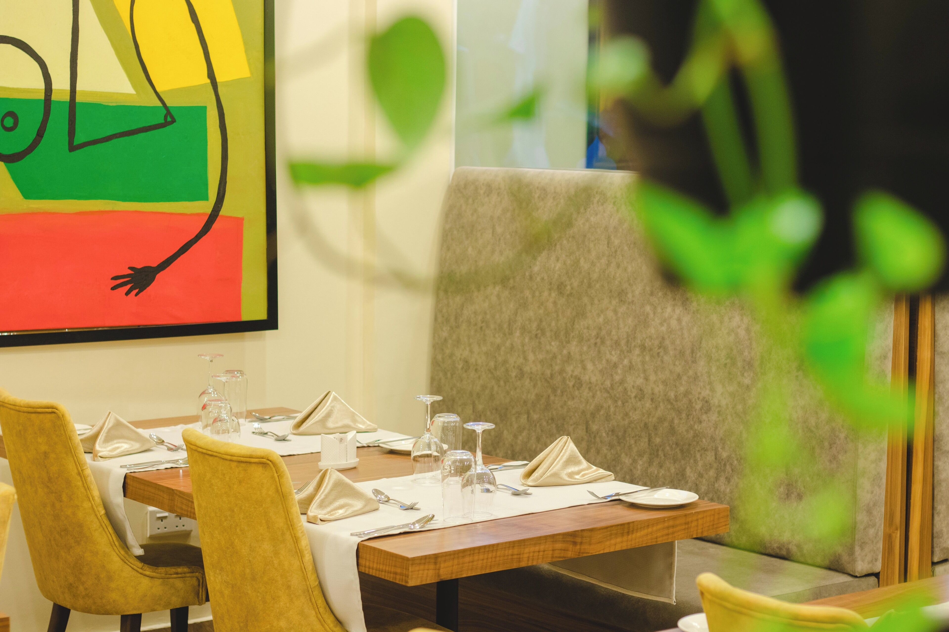 A dining area with a wooden table set for four, upholstered chairs, and a large abstract painting on the wall.