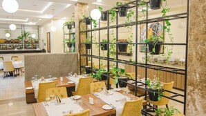 A restaurant with tables set for dining, a bar area, and a wall decorated with potted plants. - Bon Hotel Imperial (Abuja)