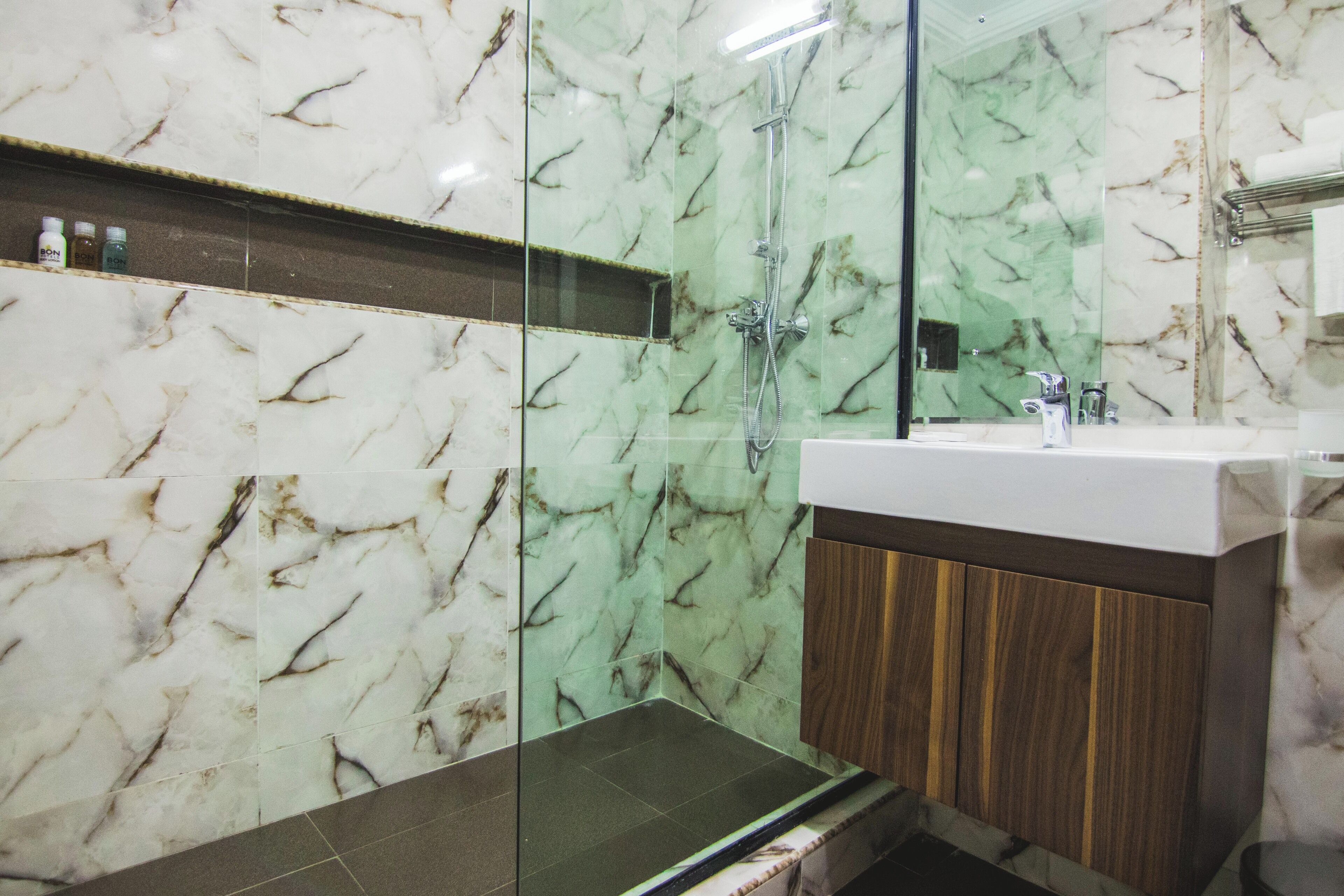 Un baño con ducha de vidrio, tocador con encimera de mármol y un armario de madera.