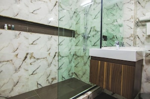 Un baño con ducha de vidrio, tocador con encimera de mármol y un armario de madera.