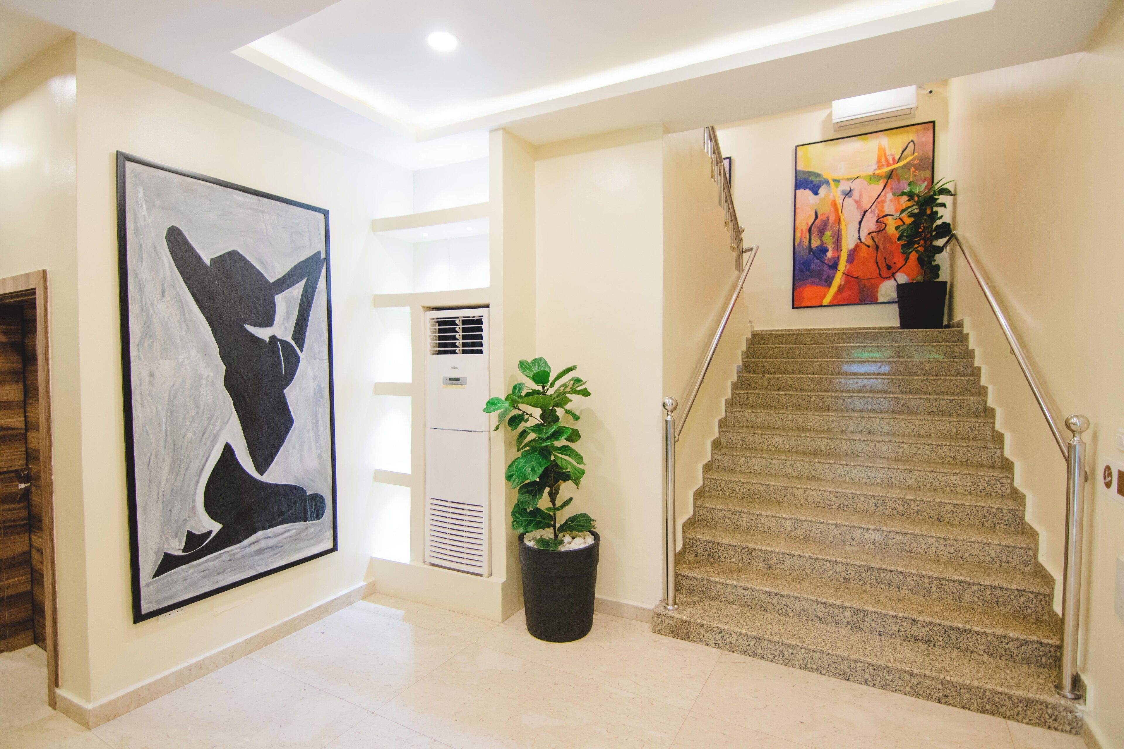 Un interior moderno con una escalera, un cuadro abstracto grande y una planta en maceta.