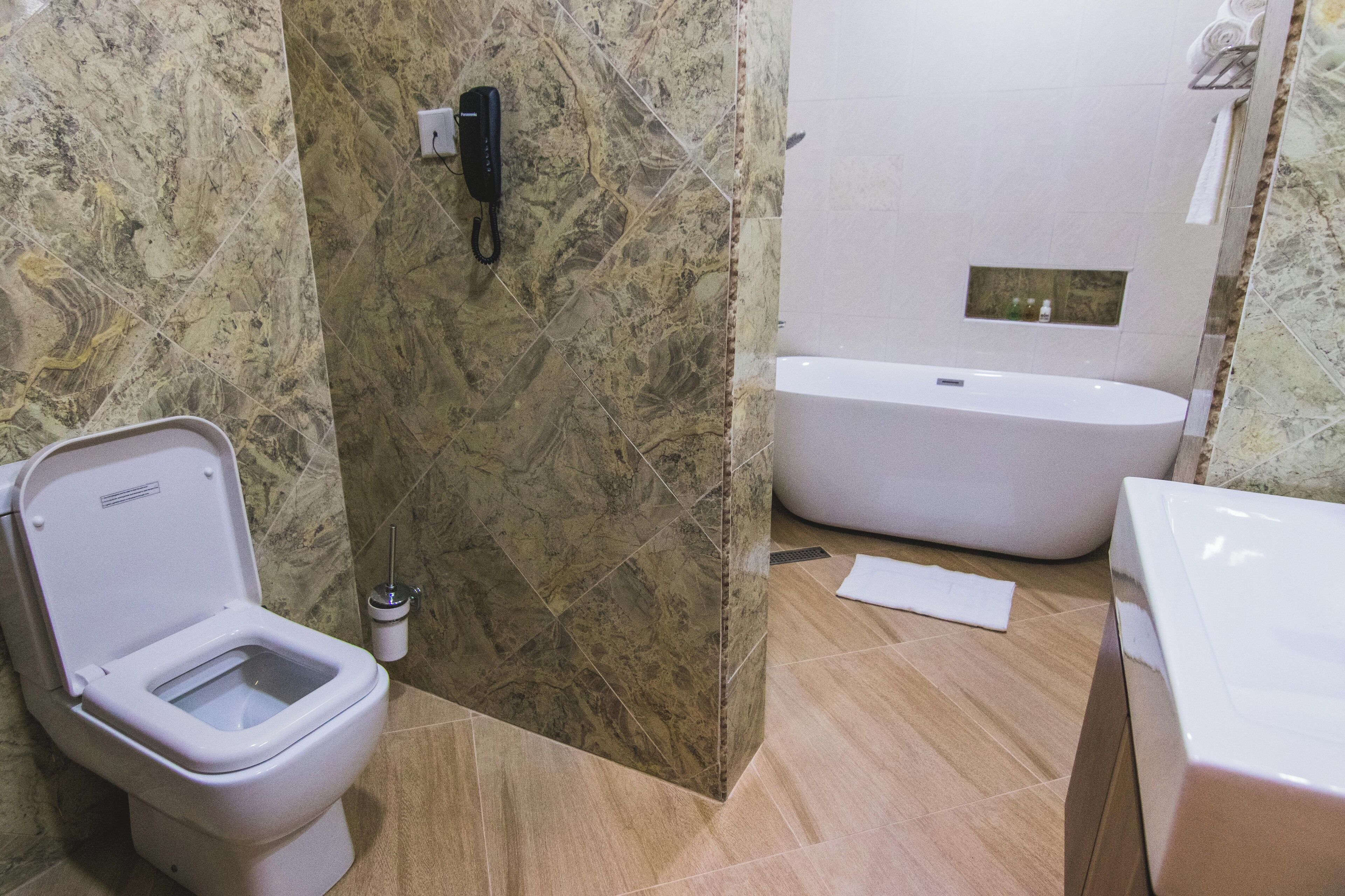 A bathroom with a toilet, a bidet, a bathtub, and a marble wall.