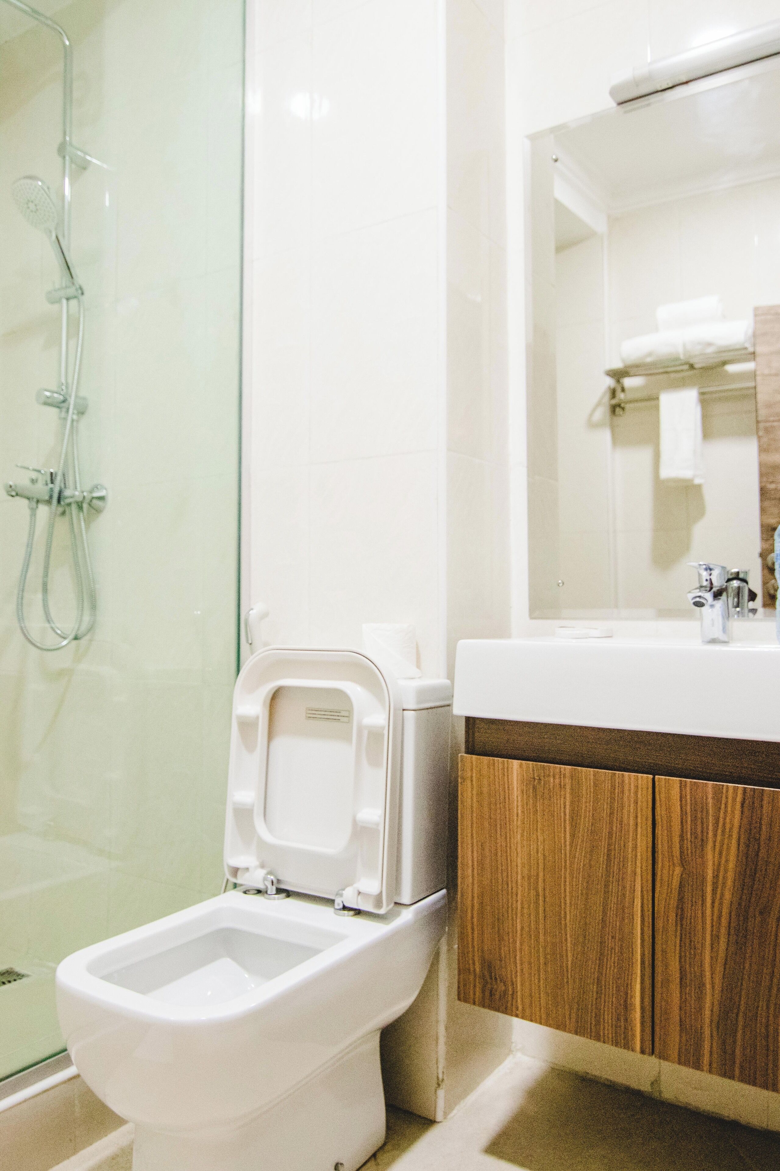A modern bathroom with a glass shower enclosure, a white toilet, and a wooden vanity with a mirror.