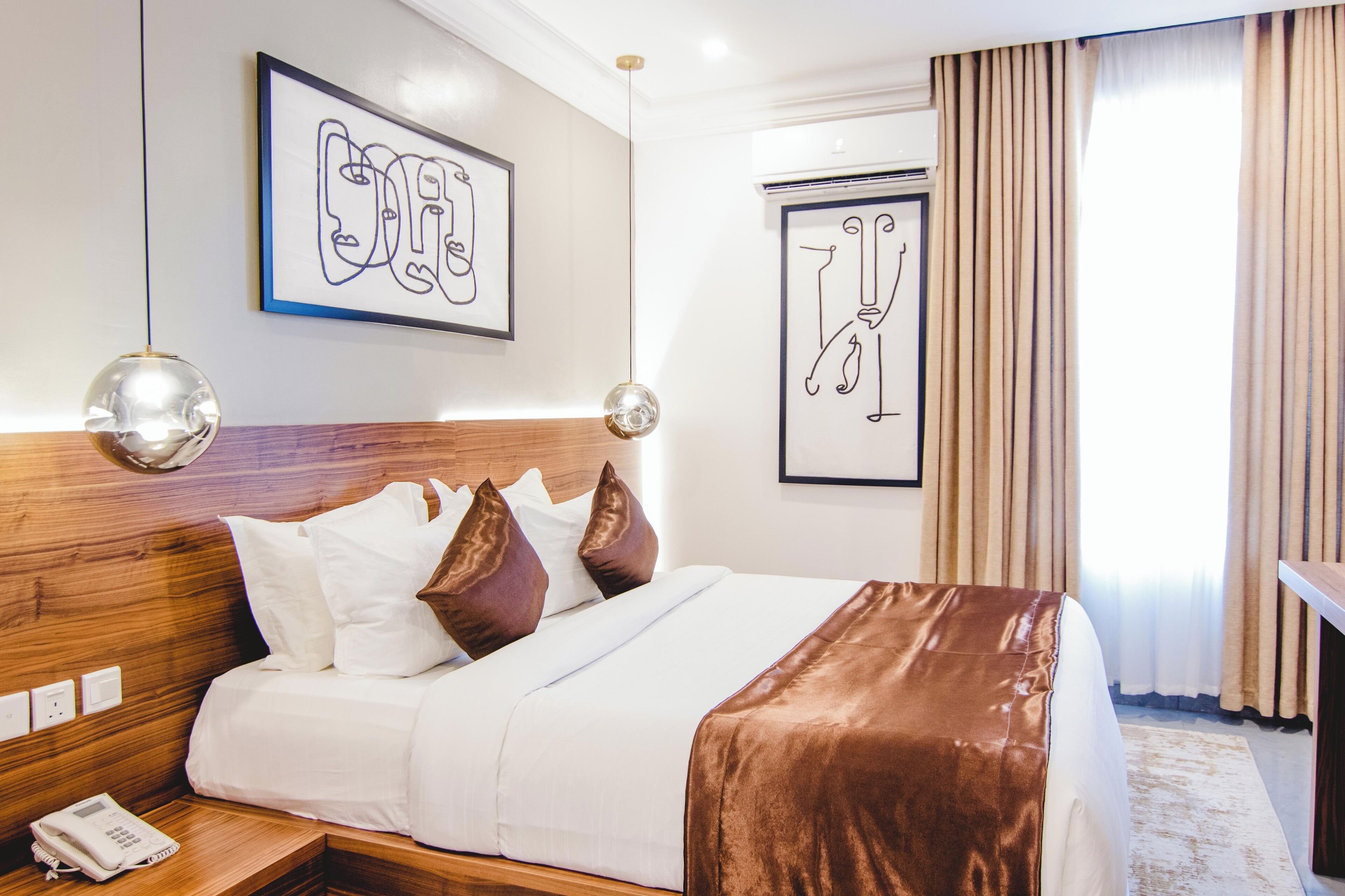 A hotel room with a wooden headboard, white bedding, brown throw blanket, and artwork on the walls.