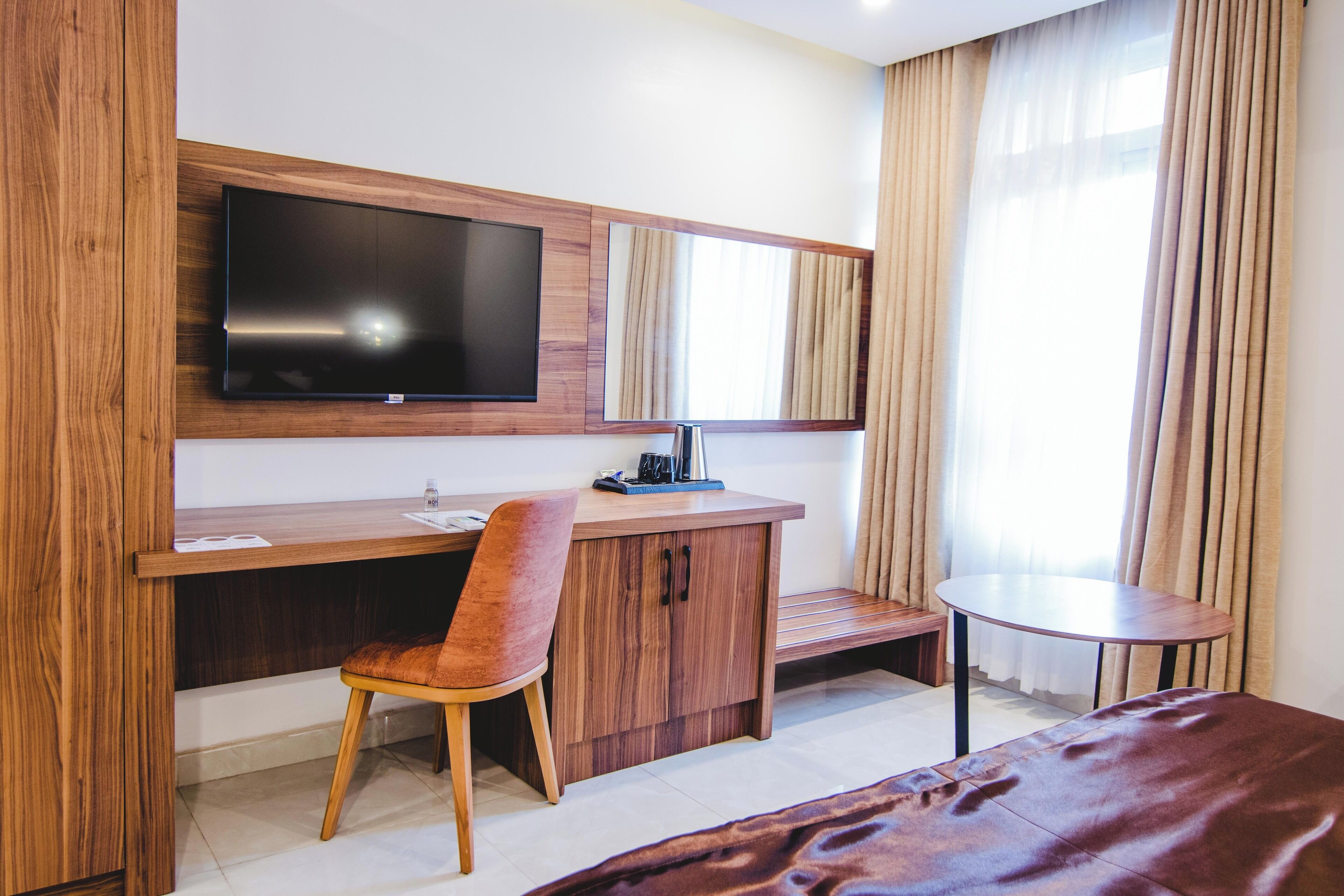 Habitación de hotel con escritorio de madera, una silla, televisor montado en la pared, una mesita redonda y una cama.