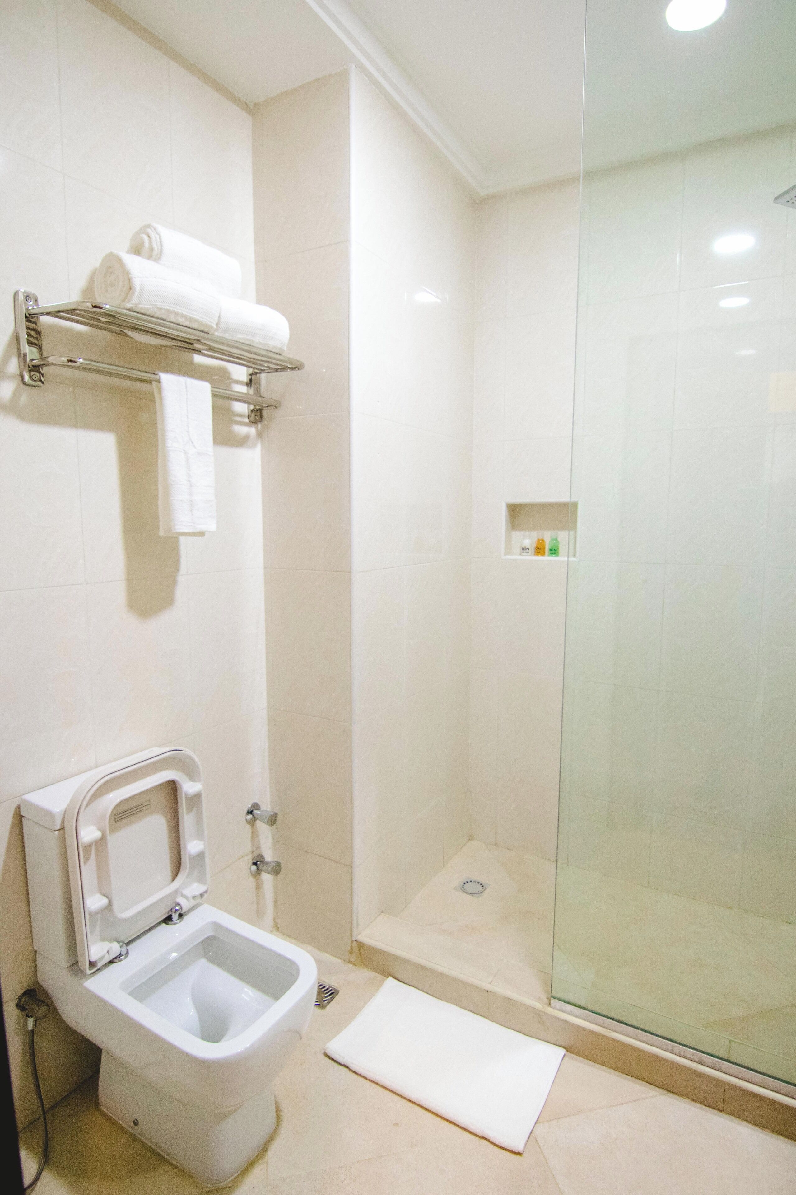 A modern bathroom with a glass-enclosed shower, a toilet with a bidet attachment, and a shelf with towels.