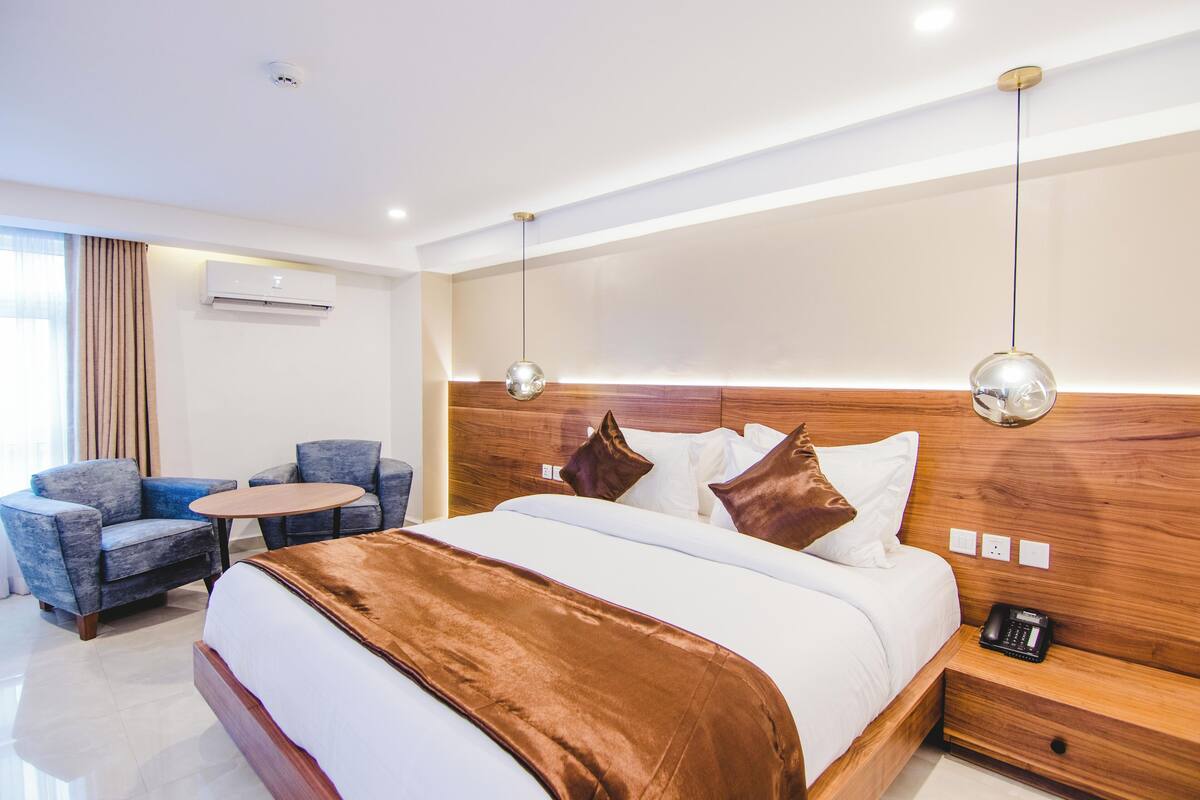 Habitación de hotel con cama, dos sillones, una mesita, una mesita de noche con teléfono y un equipo de aire acondicionado.