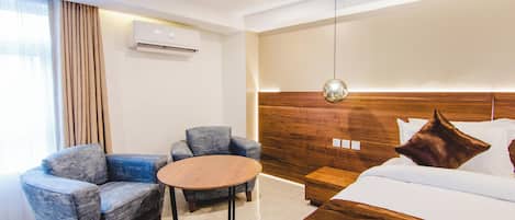 Una moderna camera d'hotel con un letto, due poltrone, un piccolo tavolo rotondo, una testiera in legno e un condizionatore d'aria.