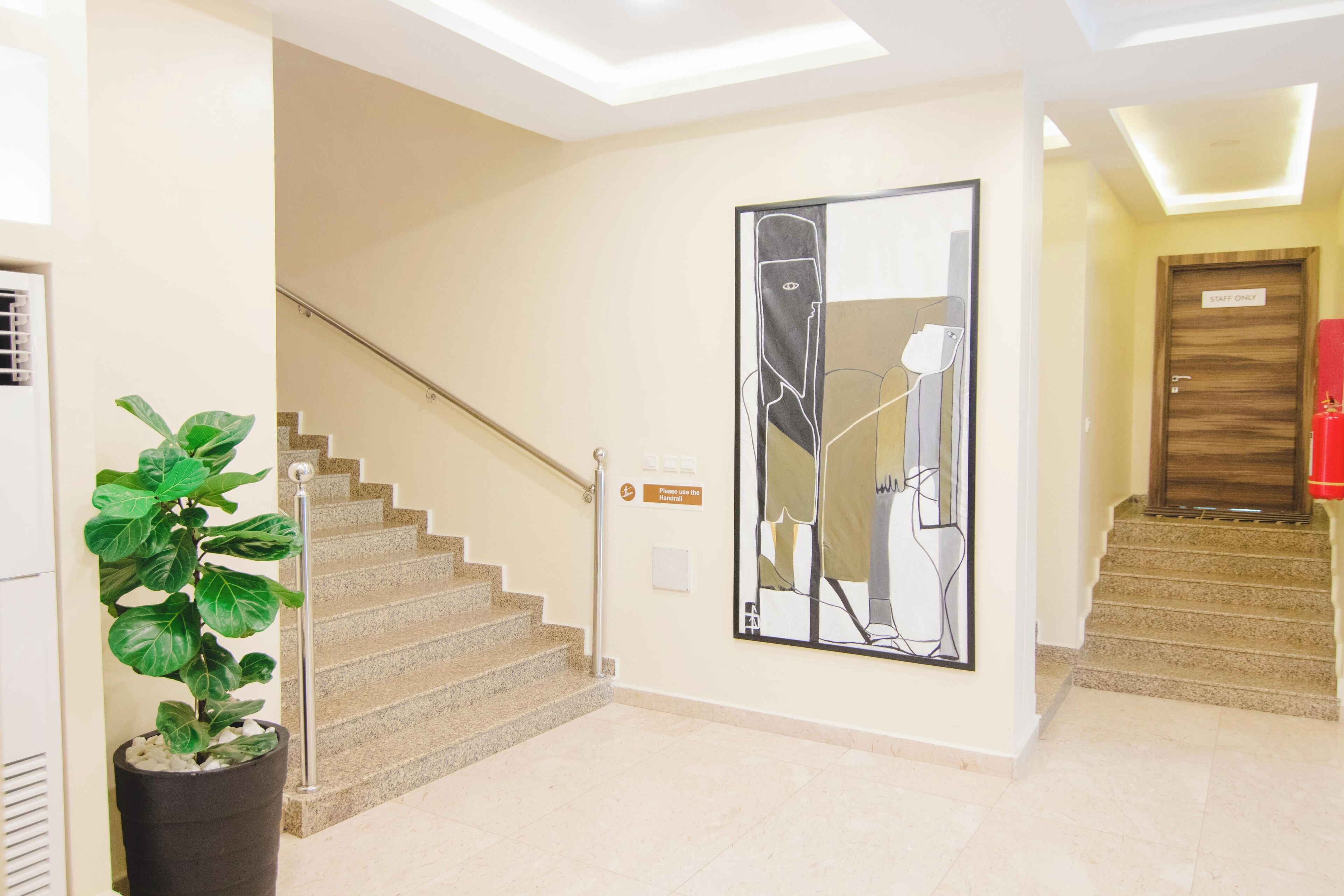 Vestíbulo de hotel con una escalera, un cuadro abstracto de gran tamaño, una planta en maceta y una puerta que indica 'Solo personal'.