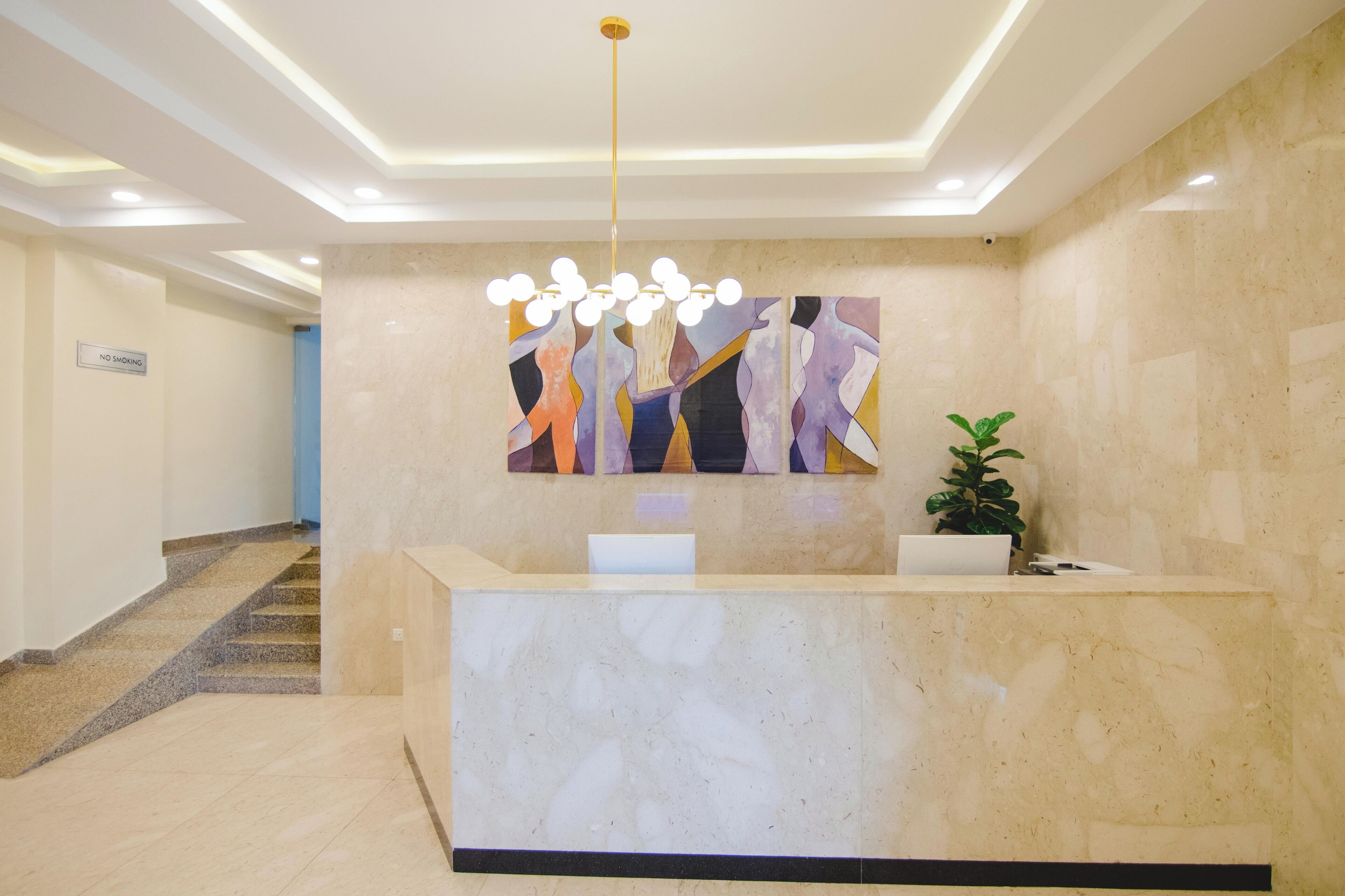 Et hotellets reception område med en skrivebord i marmor, et skilt med 'No Smoking', et moderne abstrakt maleri og en lampe i loftet.