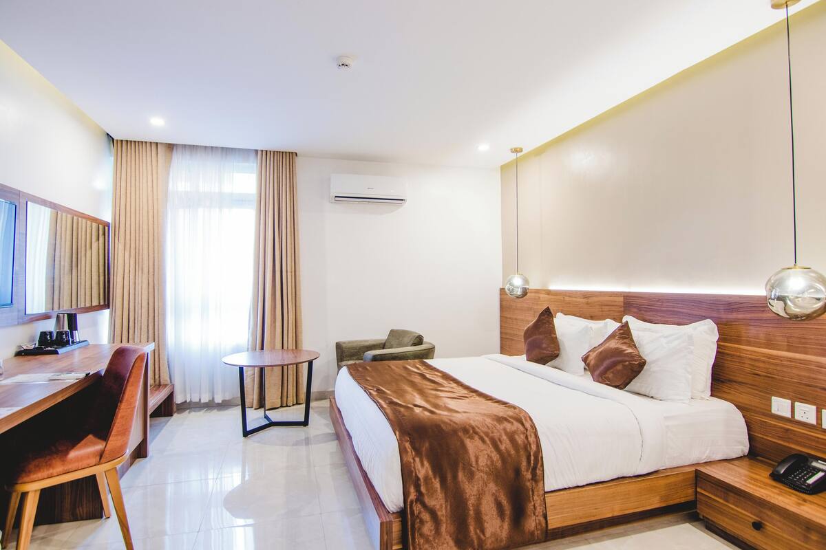 Una habitación de hotel con cama, mesita de noche, escritorio, silla y una pequeña mesa redonda.