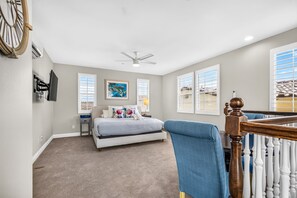 A bedroom with a bed, a ceiling fan, a TV, and a window with blinds.