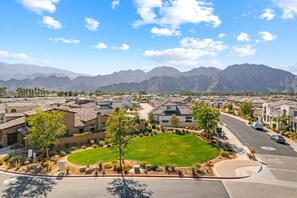 A residential area with houses, a green lawn, and mountains in the background.